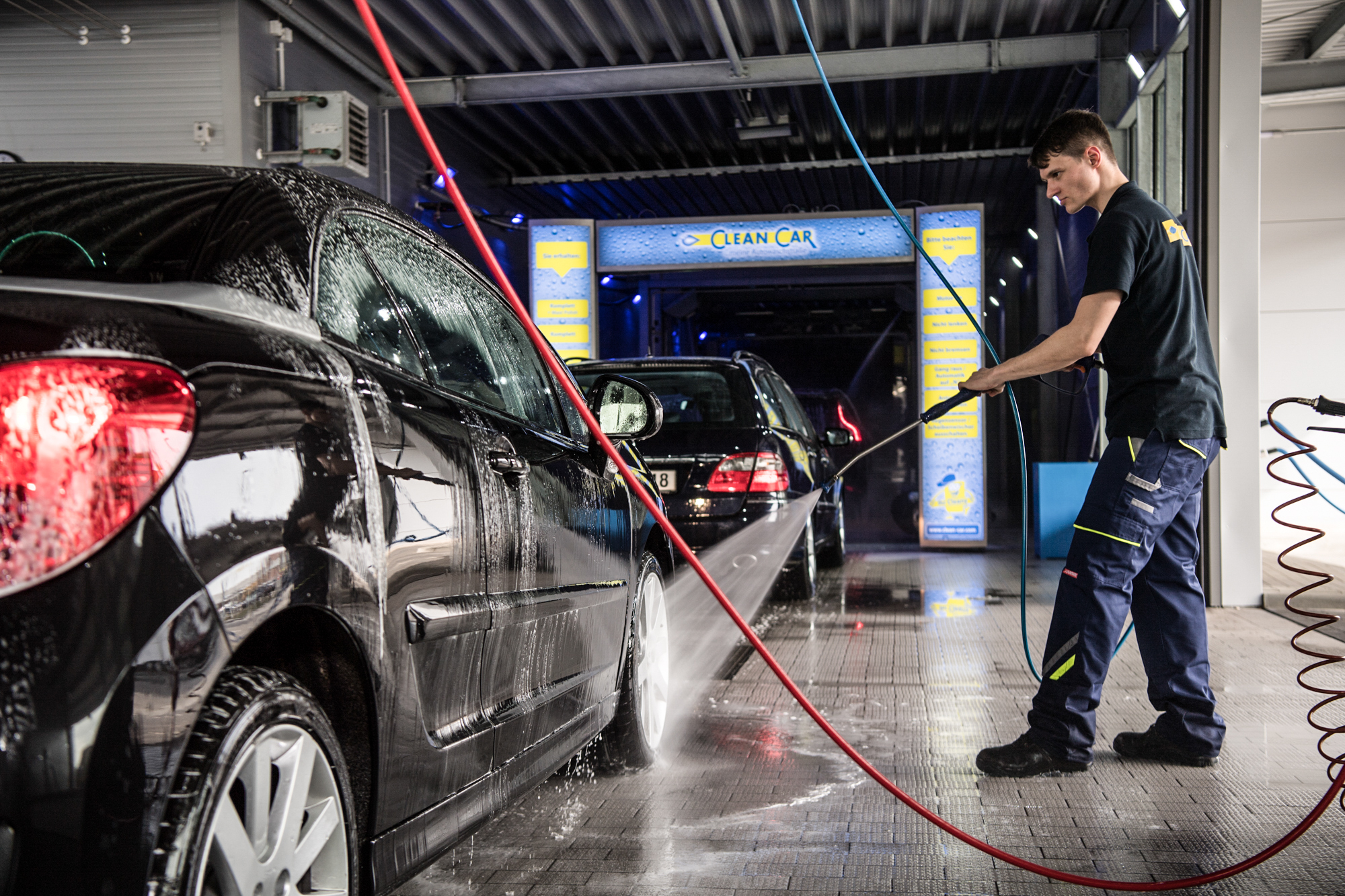 Mitarbeiter wäscht Auto in Waschstraße mit Hochdruckreiniger