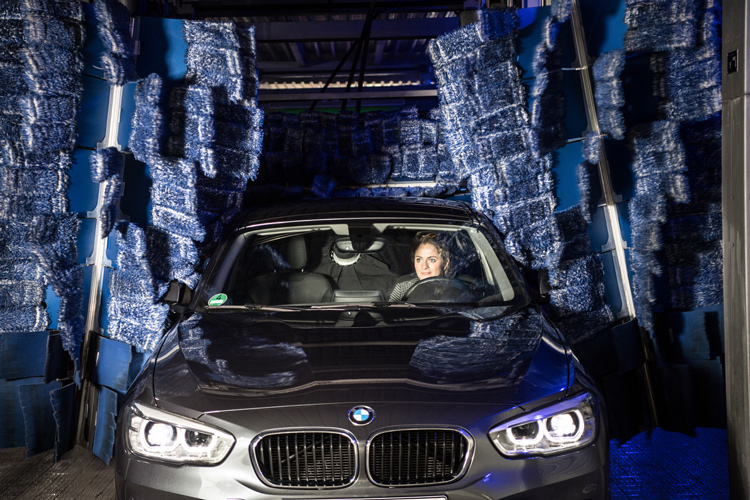 Frau fährt mit grauem Auto in die Waschstraße, wo das Auto gerade getrocknet wird